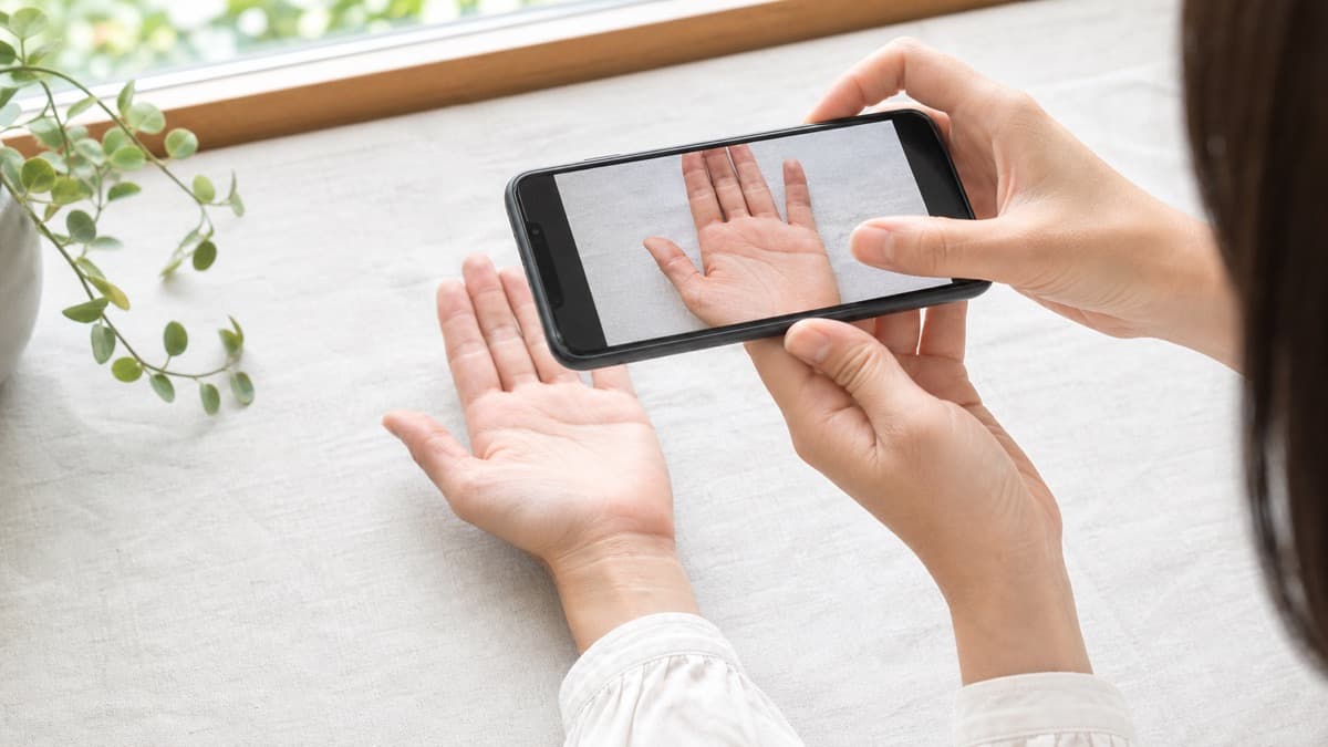 窓辺でスマートフォンを使って手のひらを真上から撮影する様子
